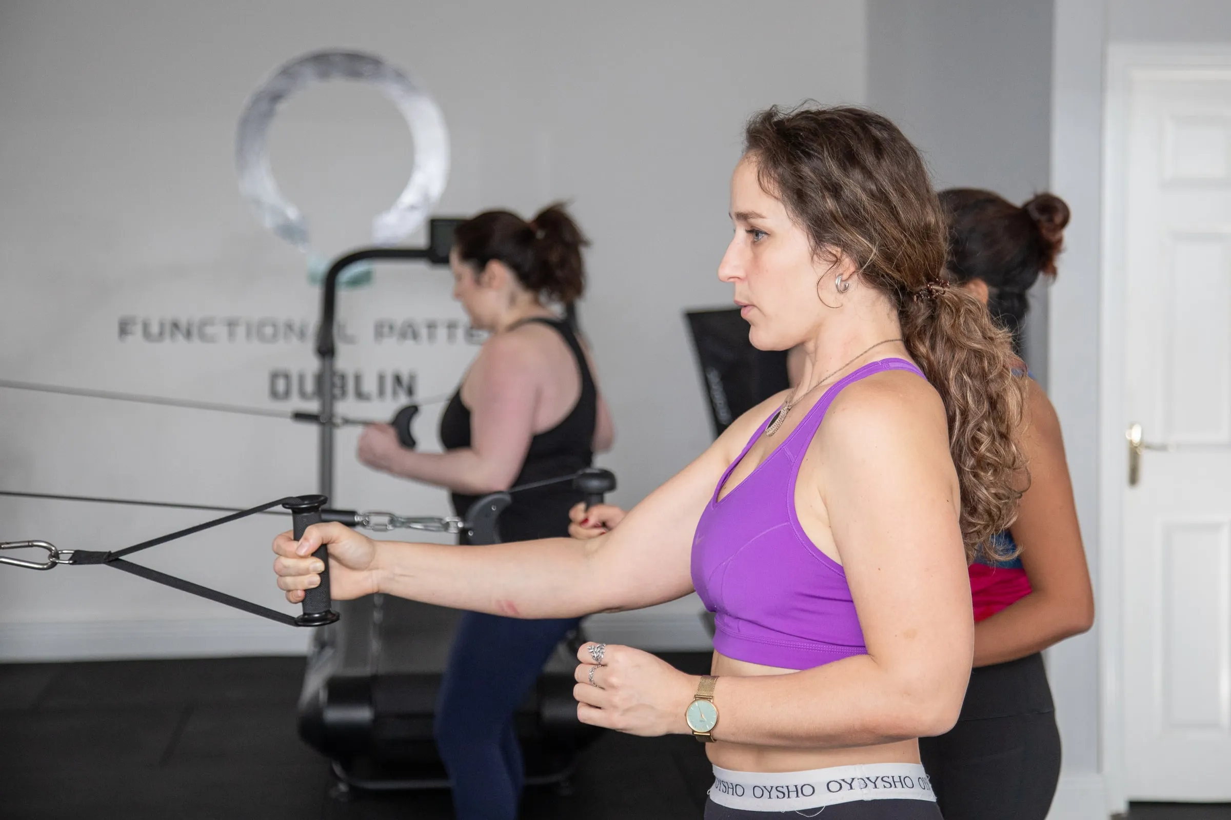 A practitioner coaching a client on the cable machine in a class